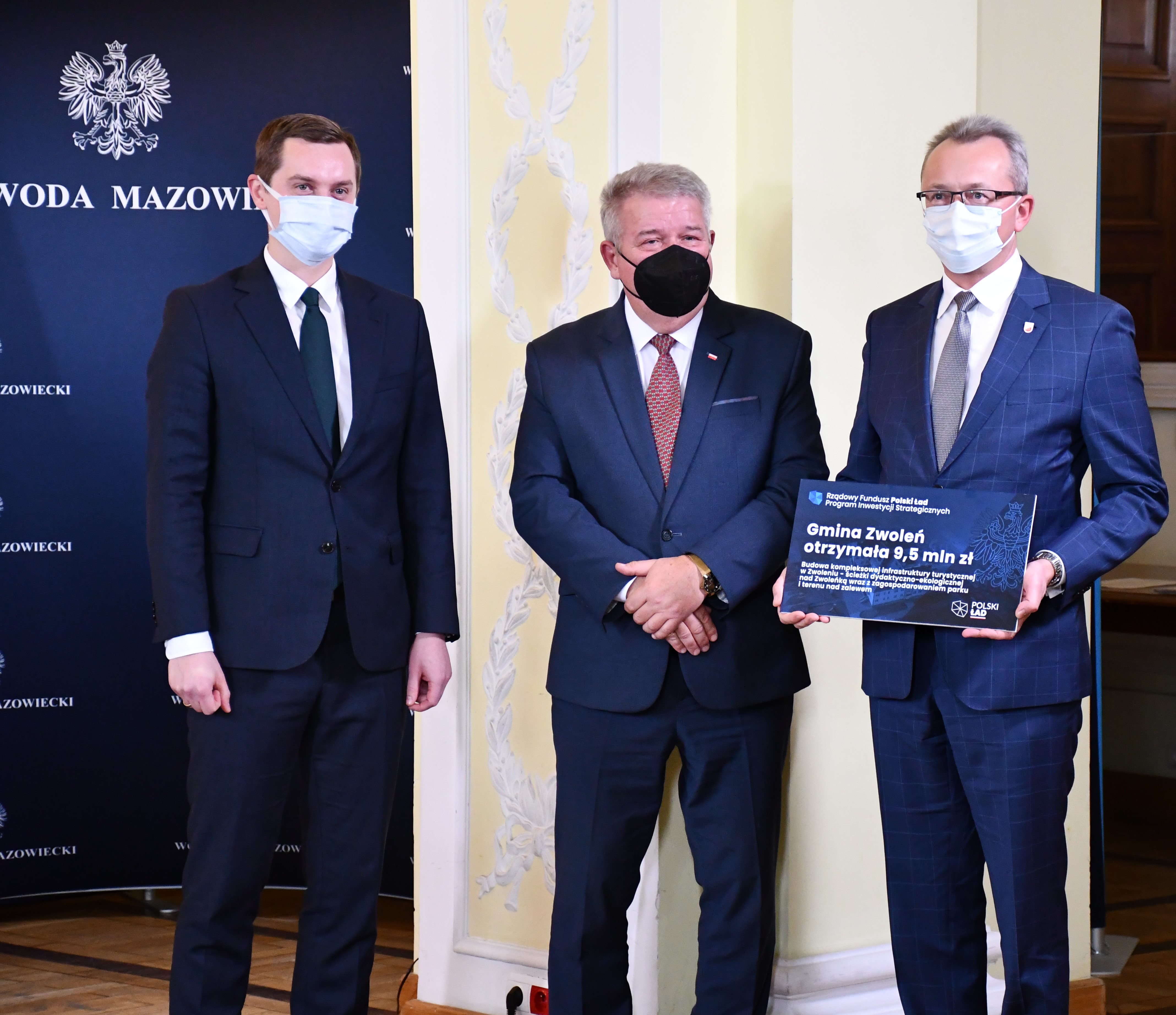 Burmistrz Zwolenia Arkadiusz Sulima trzyma wręczony przez Wicewojewodę Mazowieckiego Sylwestra Dąbrowskiego symboliczny czek. Na zdjęciu również poseł na Sejm RP Sebastian Kaleta.